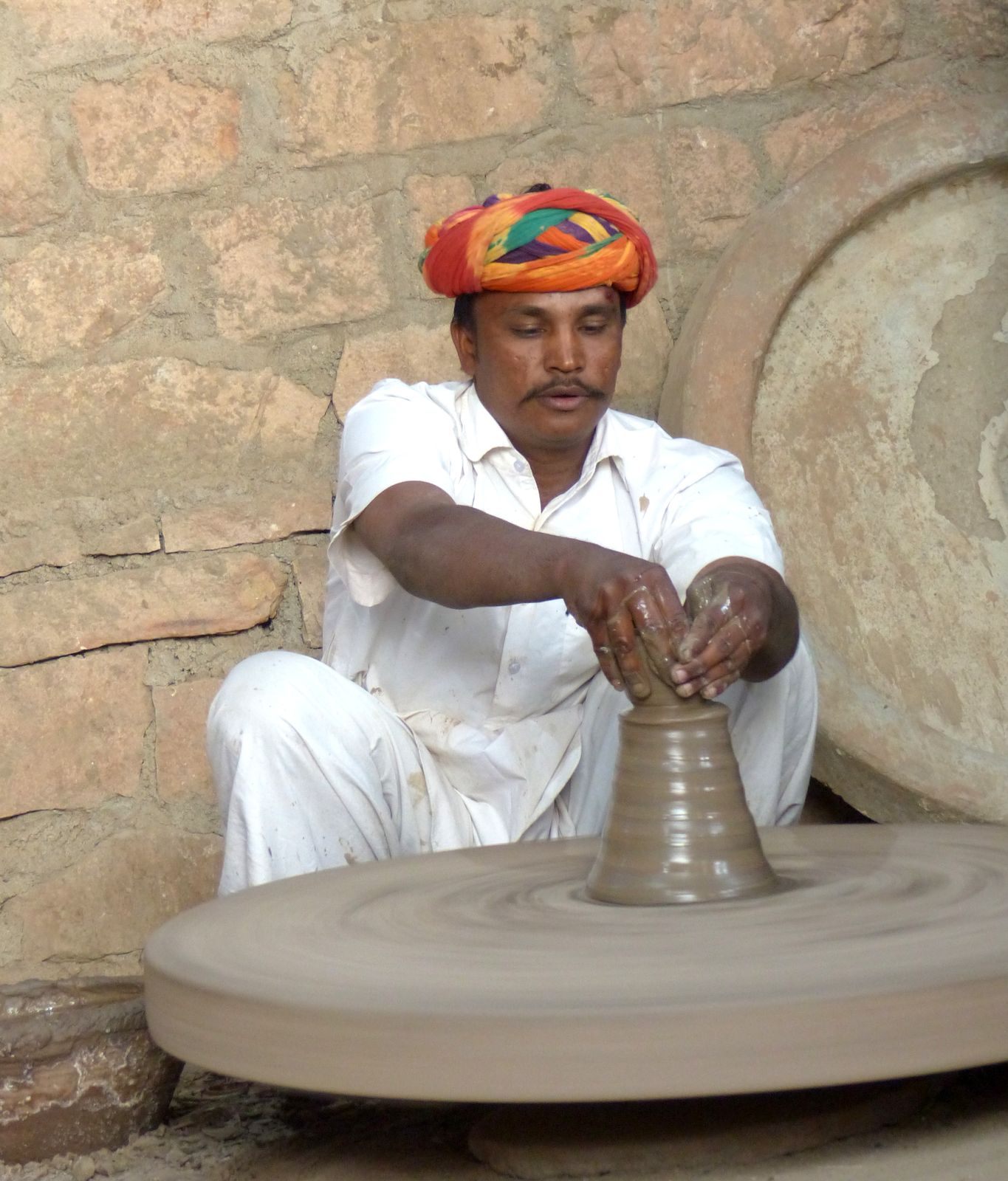 A Bishnoi potter in a turban shaping clay at his wheel