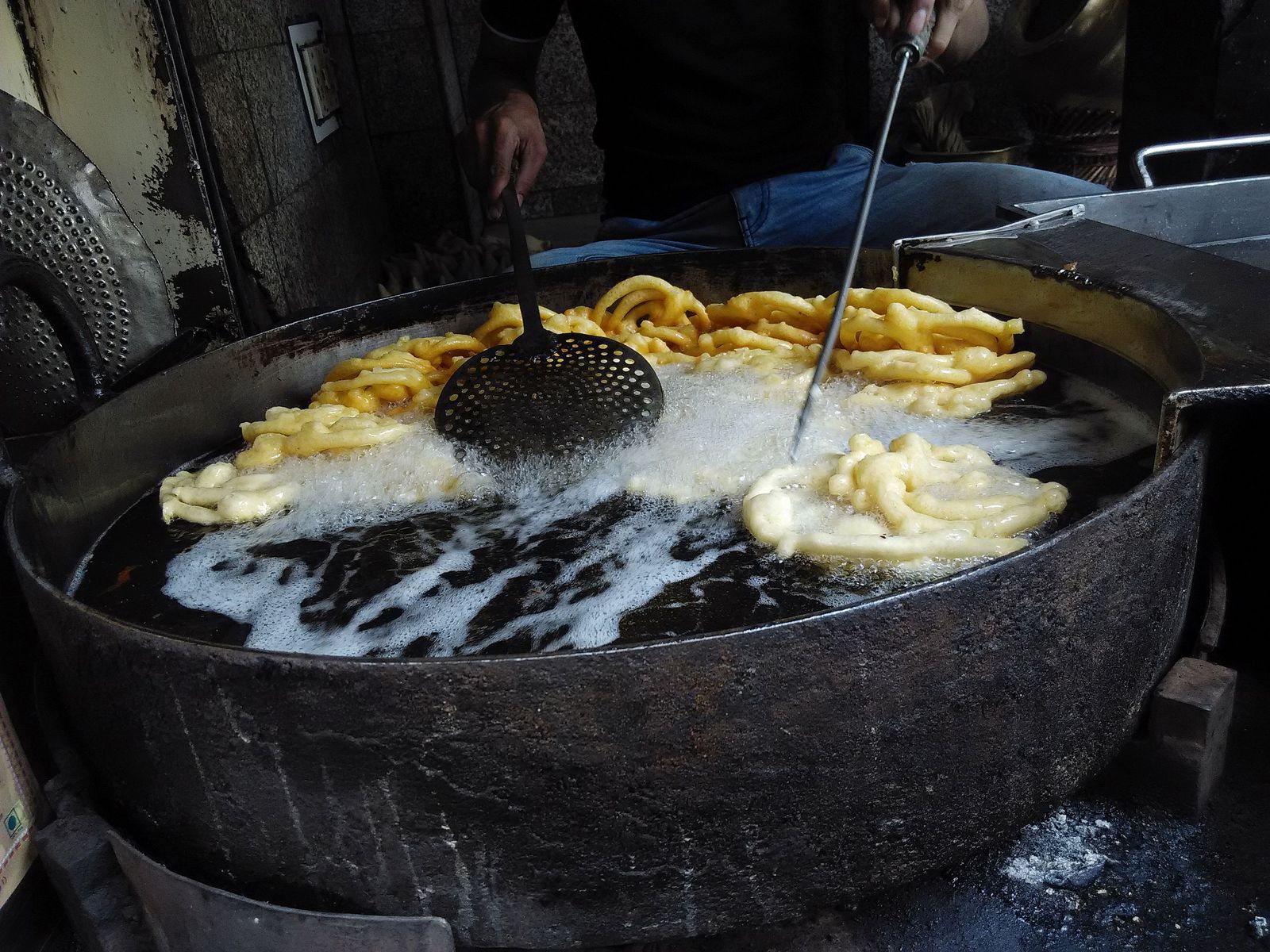 Hot orange jalebi spirals frying in a wide pan of oil in Old Delhi