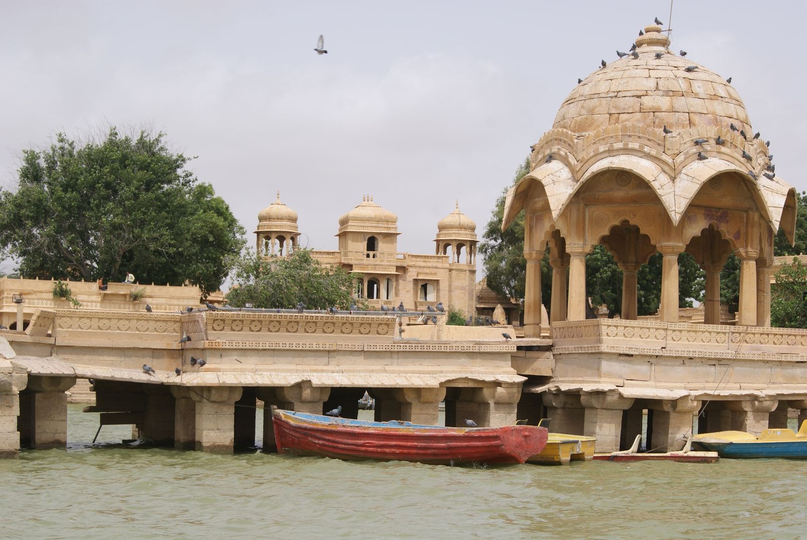 A carved stone chhatri pavilion reflected in the still water of Gadisar Lake in the early morning