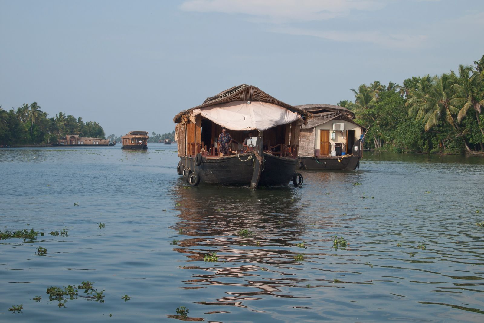 A wooden houseboat moving along a palm-lined backwater canal in Kerala in soft morning light