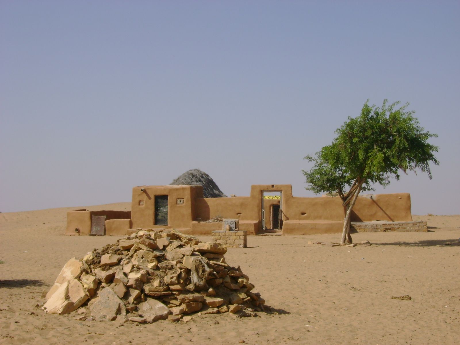A round mud-walled house with a thatched roof in a desert village near Khuri