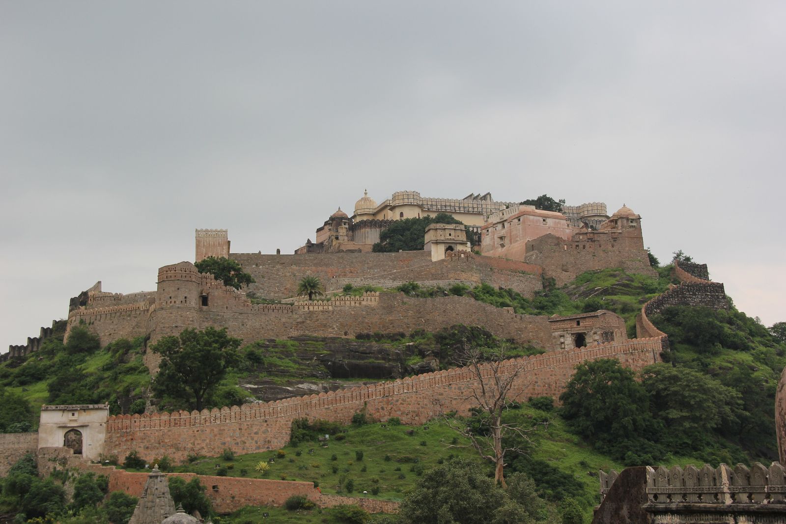 The walls of Kumbhalgarh Fort winding over green Aravalli hills under monsoon cloud