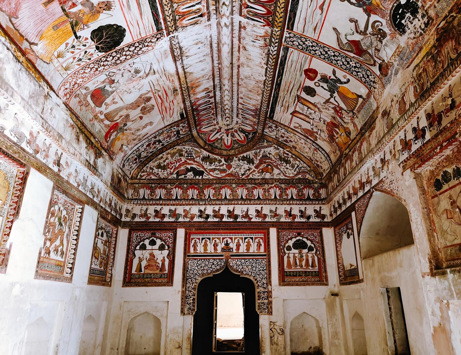 Faded wall paintings of gods, processions and court scenes inside the Raja Mahal at Orchha