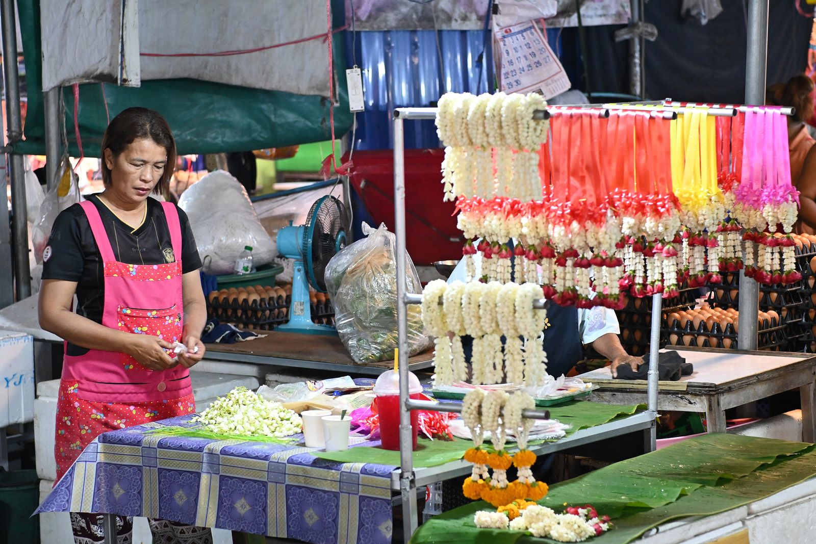 A vendor stringing fresh flower garlands at a market stall