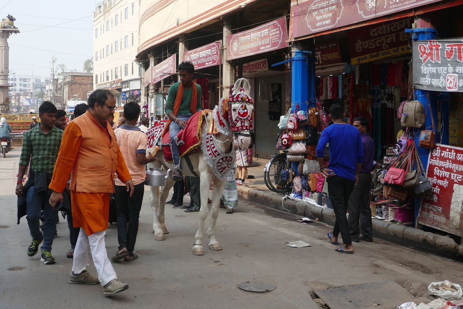 A groom on horseback leading his wedding procession, the baraat, through a bazaar