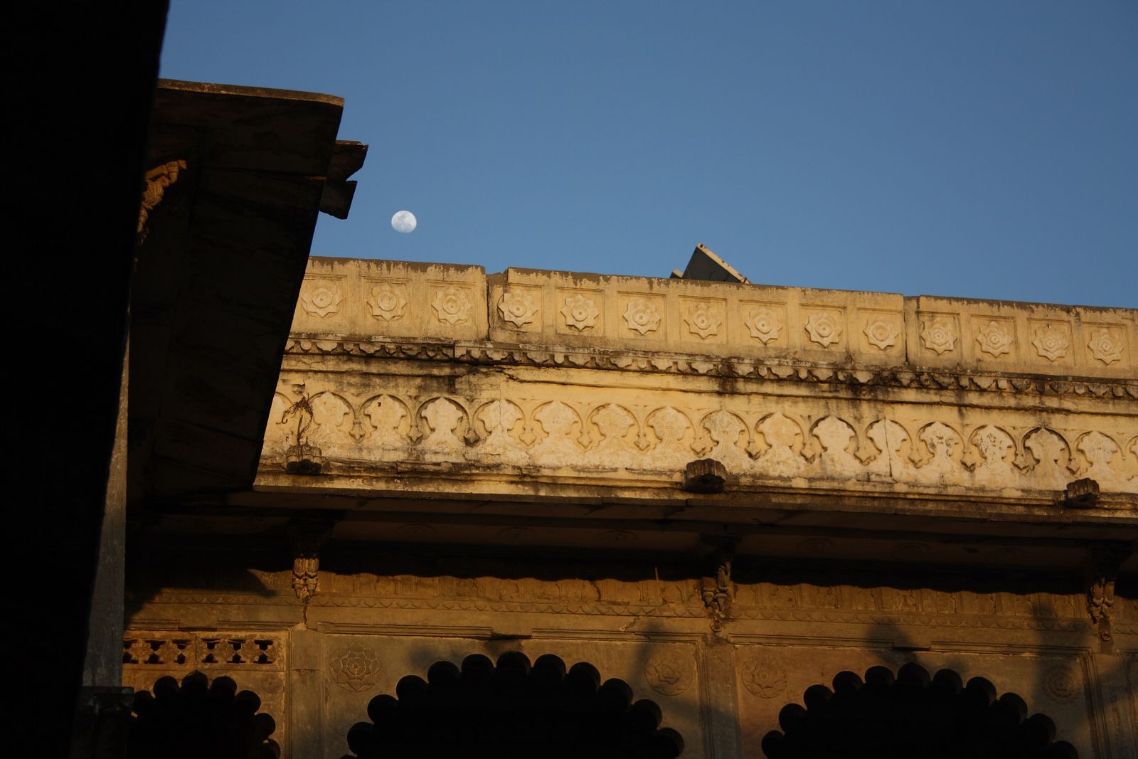 The lamp-lit inner courtyard of Bagore ki Haveli in Udaipur with a moon rising above its arches