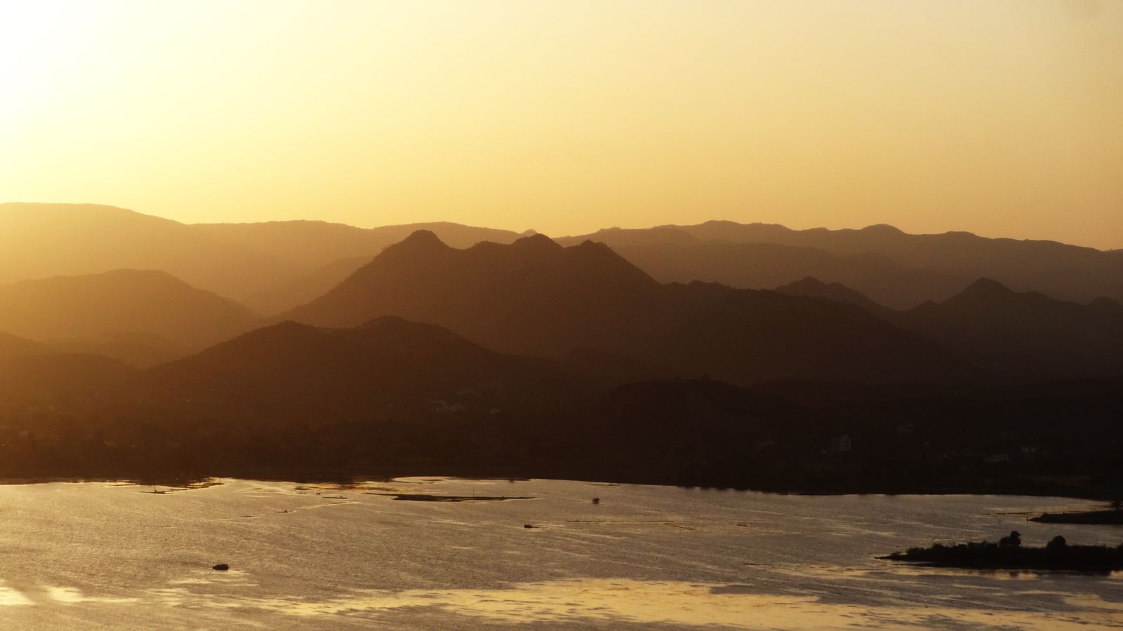 Boats on Lake Pichola in Udaipur under an orange sunset sky