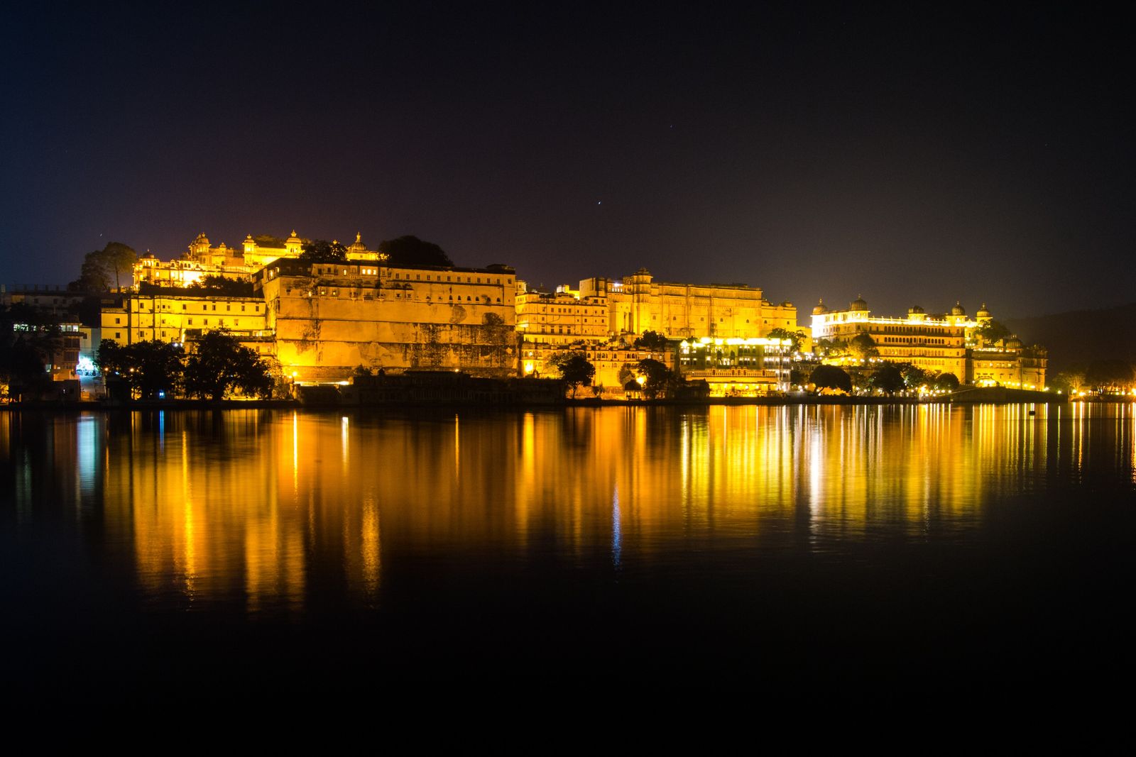 The City Palace of Udaipur lit at night, reflected in Lake Pichola